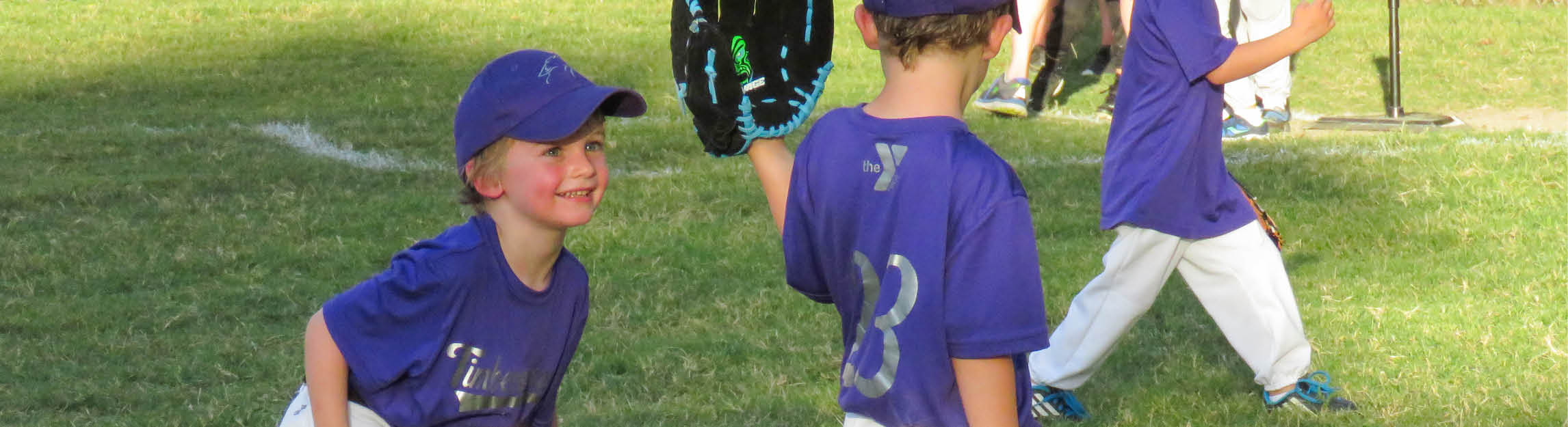 Youth Baseball participant smiling in a purple jersey and baseball cap 