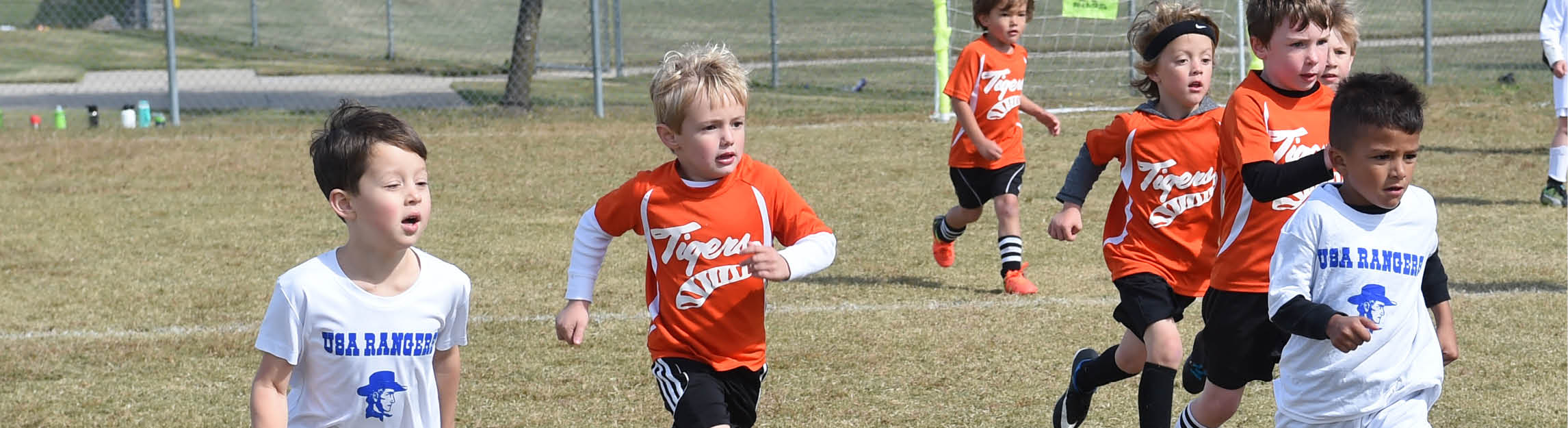 Male soccer players in white and orange jerseys running down the field
