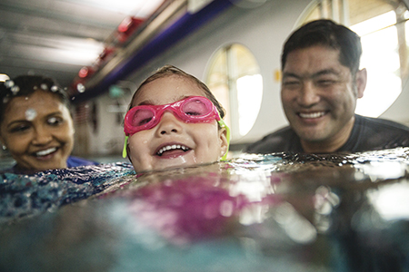 Young child swimming in an indoor pool with the help of two adults