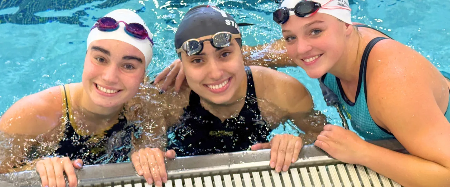 three girls in pool as part of swim team posing and smiling