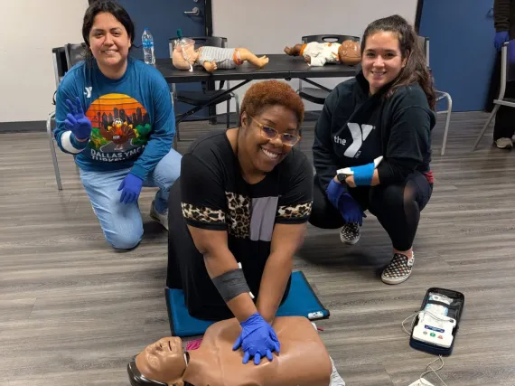 People posing while someone is performing chest compressions on a dummy during a CPR training