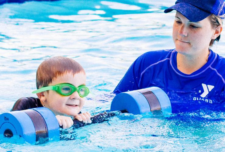 Lifeguard assisting male child during a swim lesson using a flotation device