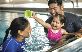 Father and daughter in a swim lesson. The daughter is playing with her instructor by pouring water on her head.