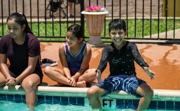 Three kids sitting by an outdoor pool