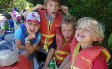 Four kids wearing life vests at a summer camp