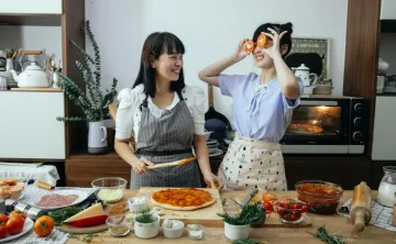 Two individuals making pizza in the kitchen 